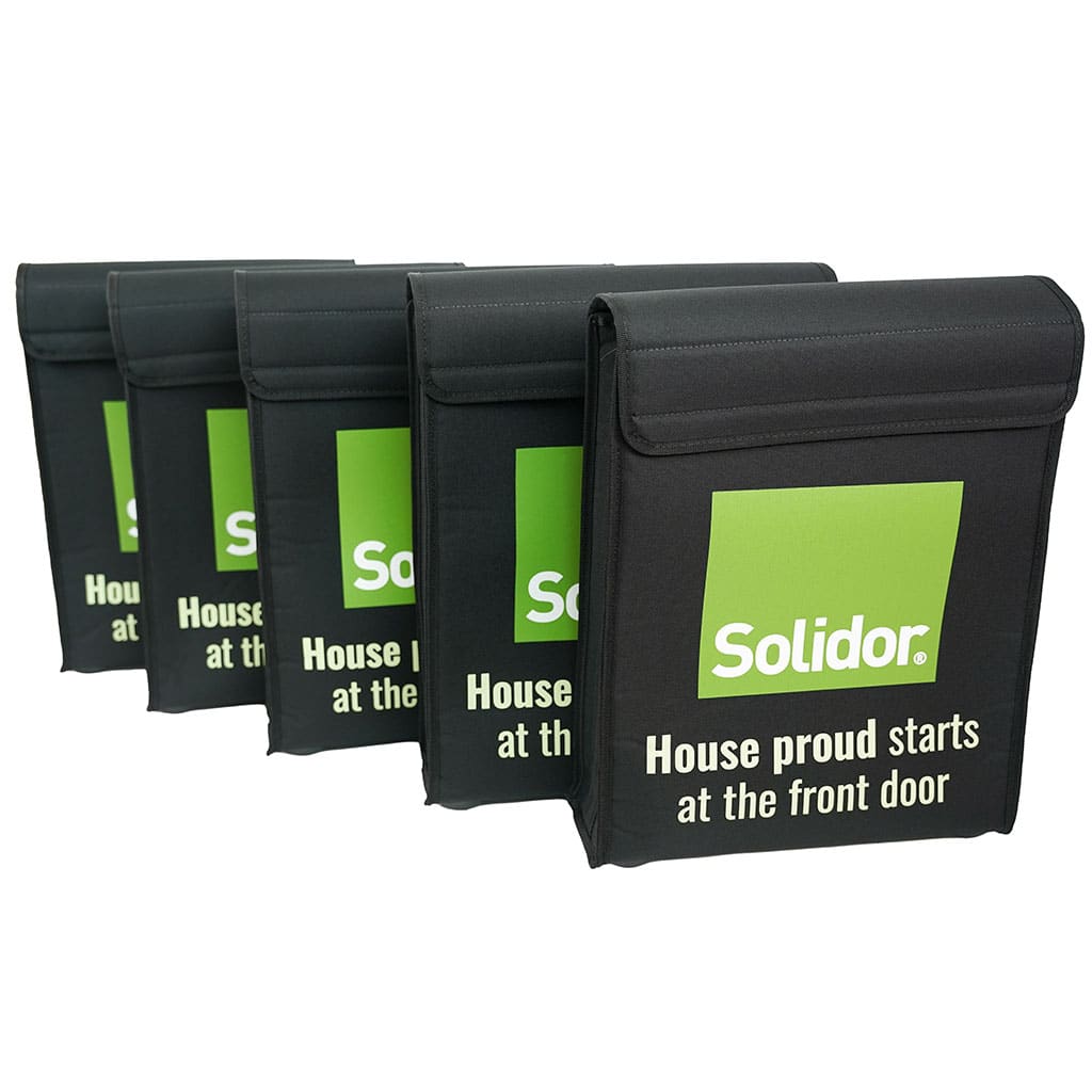 Stack of black tote bags with a green Solidor logo and the slogan 'House proud starts at the front door'.